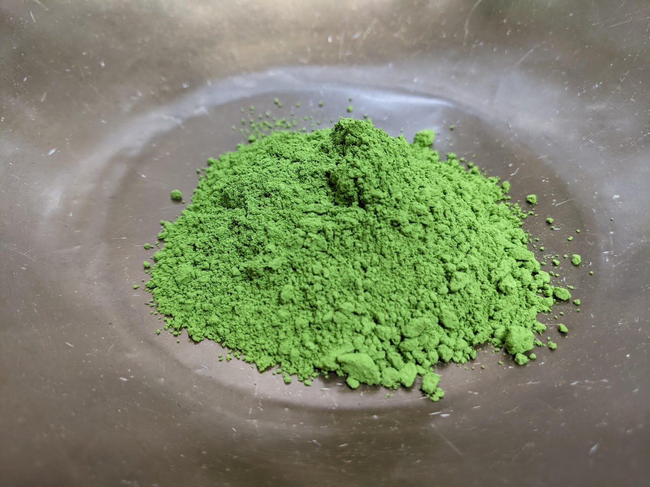 A mound of bright green Okumidori matcha powder in a metal bowl.